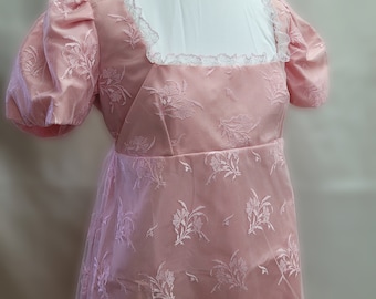 May include: A pink dress with a floral pattern and a lace neckline. The dress has short puffed sleeves and a fitted bodice.