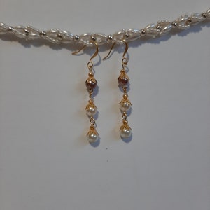 May include: A pair of gold dangle earrings with three white pearls and a brown pearl on each earring.