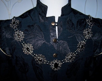 May include: A black velvet jacket with a high collar and a silver beaded necklace with black gemstones.