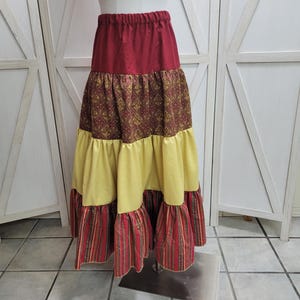 May include: A long, tiered skirt with a red top layer, a patterned brown and gold middle layer, a yellow layer, and a red and gold striped bottom layer.