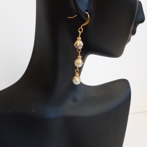May include: Gold dangle earrings with three pearl-like beads and a pink bead. The beads are separated by gold chain links.