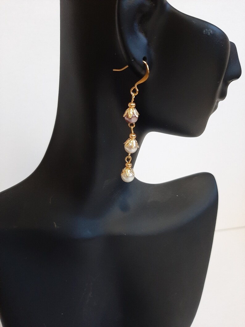 May include: Gold dangle earrings with three pearl-like beads and a pink bead. The beads are separated by gold chain links.