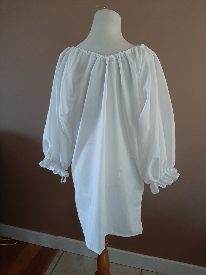 May include: White peasant blouse with long sleeves and a gathered neckline. The sleeves have ruffles at the cuffs and are tied at the wrists.