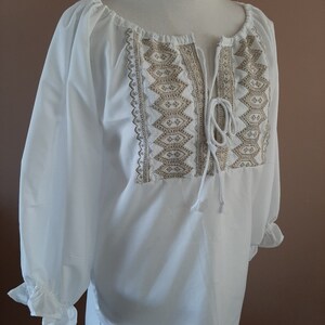 May include: White peasant blouse with a gold embroidered neckline and a tie at the neck.