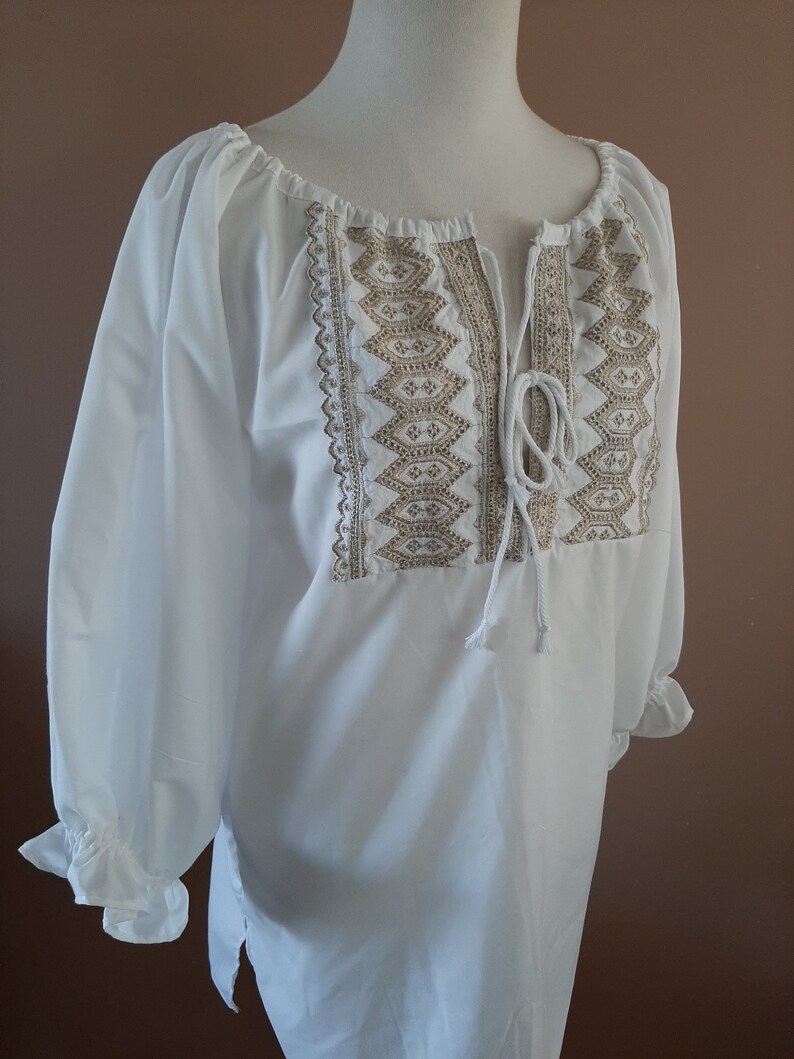 May include: White peasant blouse with a gold embroidered neckline and a tie at the neck.