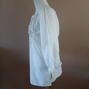 May include: White long-sleeved blouse with a lace trim around the neckline and cuffs. The blouse has a relaxed fit and a slightly longer length.