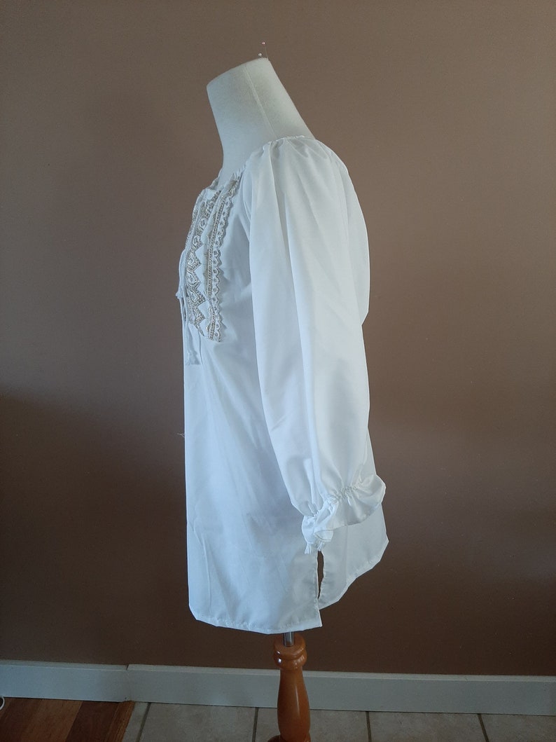 May include: White long-sleeved blouse with a lace trim around the neckline and cuffs. The blouse has a relaxed fit and a slightly longer length.