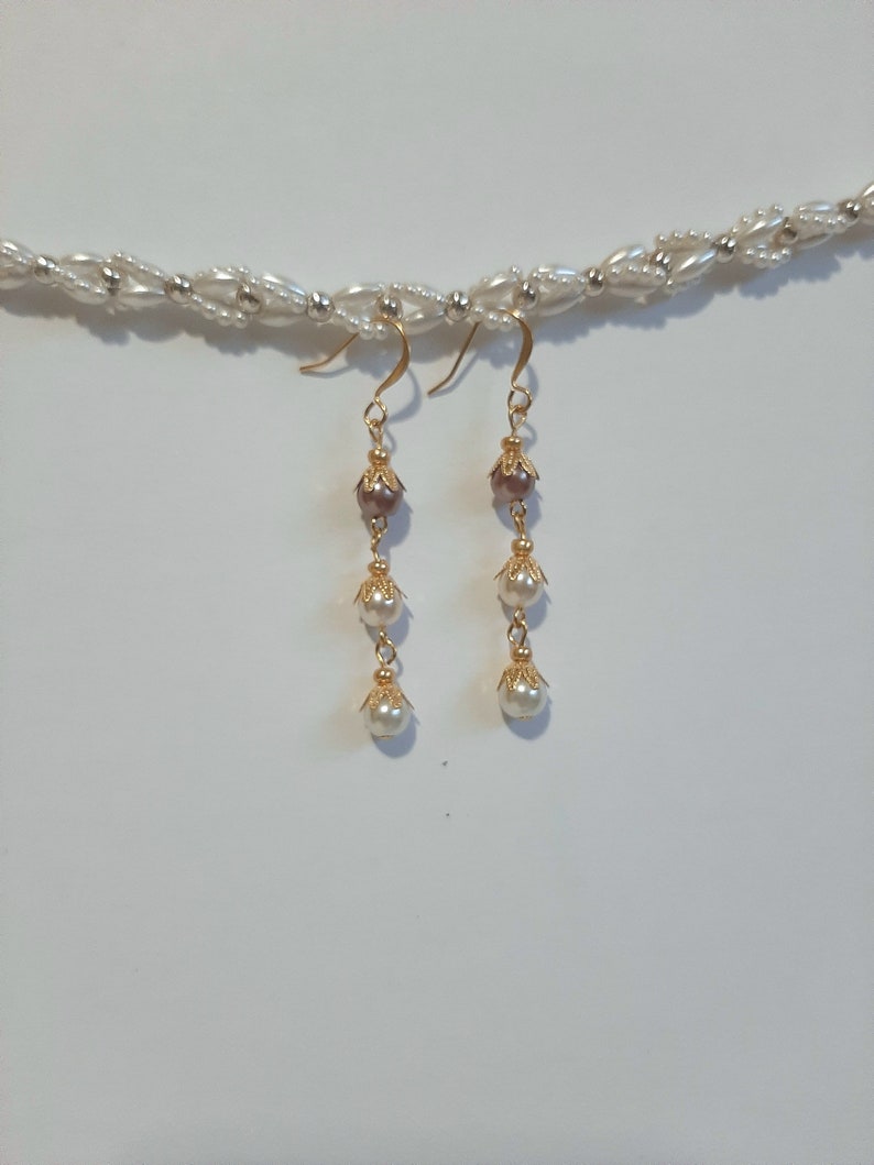 May include: Gold dangle earrings with three white pearls and a brown pearl on each earring.
