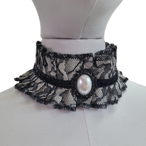 May include: A black lace choker with a white pearl accent. The choker is ruffled and has a delicate design.
