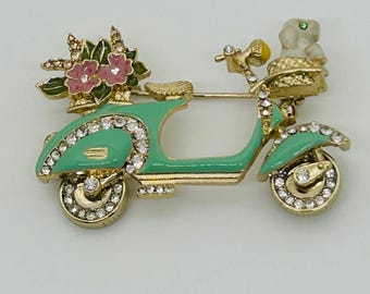 Broche de Anne Klein en esmalte verde con forma de scooter, adornado con un perro y una flor de diamantes de imitación.