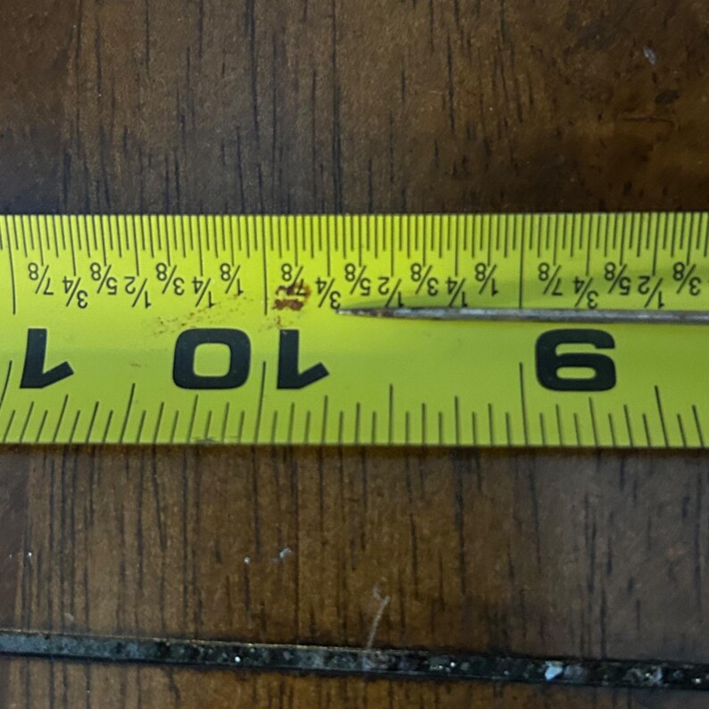 May include: A yellow tape measure with black markings and numbers. The tape measure shows a measurement of approximately 9 3/8 inches. The tape measure is lying on a dark brown wooden surface.