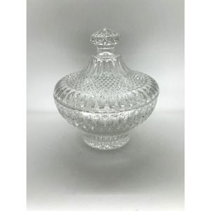 May include: A clear, cut-glass candy dish with a lid. The dish has a round, bulbous body and a diamond-patterned design. The lid is topped with a faceted knob. The dish is likely vintage and suitable for decorative use.