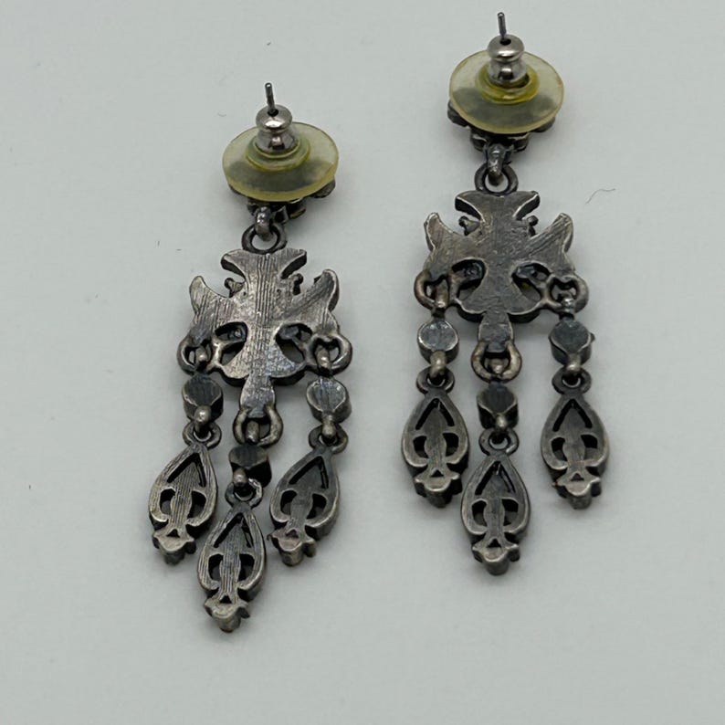 Puede incluir: Par de pendientes colgantes plateados. Cada pendiente presenta una parte superior en forma de cruz con colgantes en forma de l&aacute;grima. Los pendientes tienen una est&eacute;tica vintage o antigua, con un dise&ntilde;o detallado.