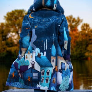 May include: A blue hooded jacket with a whimsical print of a night sky with stars, a crescent moon, and a cityscape. The jacket has a white lining and a hood with a brown lining.