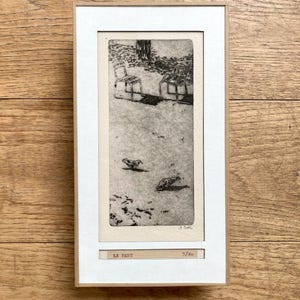 Könnte beinhalten: Ein gerahmter Schwarz-Weiß-Radierungsdruck mit dem Titel LE PARC, nummeriert 3/40. Das Kunstwerk zeigt zwei Stühle in der Nähe eines Baumes und zwei kleine Vögel auf dem Boden. Der Druck befindet sich in einem hellen Holzrahmen mit weißem Passepartout.
