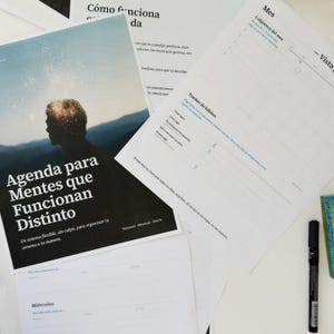 May include: A printed planner set featuring a cover with a silhouette of a person against a mountain landscape and the text Agenda para Mentes que Funcionan Distinto. Includes monthly habit tracker sheets with Spanish text and a black felt tip pen.