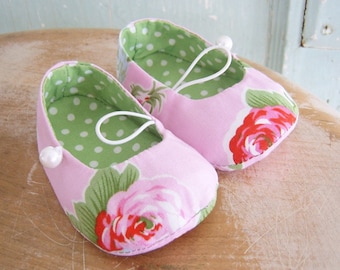 Op de afbeelding: Een paar roze babyschoentjes met een bloemenprint en witte stippen. De schoentjes hebben witte elastische bandjes en witte parel accenten.