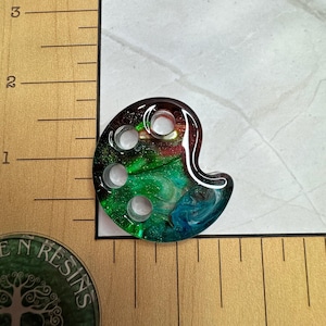 May include: A green, blue, and red resin paint palette with four holes. The palette is approximately 1.5 inches in diameter.
