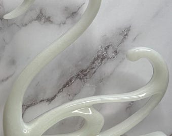 May include: A white ceramic swan sculpture with a glossy finish. The swan has a long neck and its wings are spread out.
