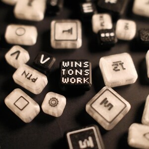 Puede incluir: Un conjunto de teclas de teclado de ordenador, algunas negras y otras blancas, dispersas sobre una superficie oscura. Una tecla dice "WINS TONS WORK". Otras teclas muestran símbolos y letras como "PAGE", "10" y "V".