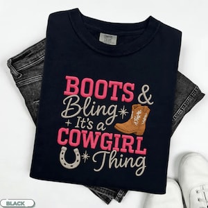 May include: Black t-shirt with the embroidered phrase "BOOTS & Bling It's a COWGIRL Thing" in pink and white. The design includes a brown cowboy boot and a horseshoe. The shirt is paired with black jeans and white sneakers.
