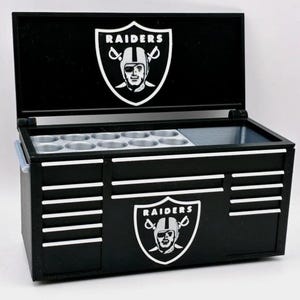 Può includere: Contenitore termico nero e bianco a tema Raiders con coperchio incernierato. Il contenitore termico presenta il logo dei Raiders sul coperchio e sulla parte anteriore. Ha un vano per le bevande e una sezione per il ghiaccio.