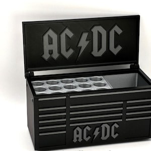 Può includere: Contenitore termico nero in stile cassetta degli attrezzi con il logo AC/DC in grigio sul coperchio e sulla parte anteriore. Il contenitore termico ha un coperchio incernierato e più cassetti. L'interno presenta un vano per il ghiaccio e una sezione con supporti circolari.
