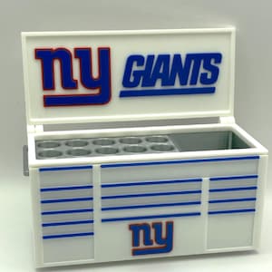 Può includere: Contenitore termico bianco e blu a tema New York Giants con il logo e il nome della squadra. Il contenitore ha un coperchio incernierato e un vano con più aperture circolari. Il contenitore misura circa 25 cm di larghezza e 20 cm di altezza.