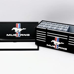 May include: Black wooden organizer with the Mustang logo, featuring a white running horse, red, white, and blue stripes, and the word "MUSTANG." The organizer has multiple circular compartments and a rectangular section.