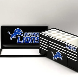 Può includere: Organizzatore a tema Detroit Lions in bianco e nero con coperchio incernierato e scatola separata con più fori. Il logo e il nome della squadra dei Detroit Lions sono visualizzati in blu e bianco.