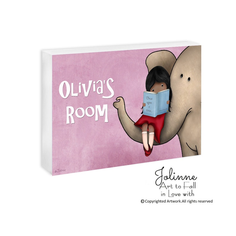 Op de afbeelding: Een roze en wit bord met de tekst "Olivia's Room" in witte letters. Een cartoonmeisje met bruin haar zit op een grijze olifant en leest een blauw boek met de tekst "Once upon a time..." Het bord is een schattige en fantasierijke toevoeging aan een kinderkamer.