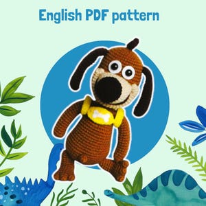 Peut inclure: Un jouet en forme de chien marron crocheté avec des oreilles noires, un museau beige et un harnais jaune avec un os blanc. Le texte "English PDF pattern" est en haut. Le fond présente un cercle bleu, des feuilles vertes et des illustrations de dinosaures bleus.
