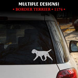 May include: A white vinyl decal of a Border Terrier in a walking pose applied to the rear window of a vehicle. The text above the decal reads MULTIPLE DESIGNS! BORDER TERRIER 1174 in white and red lettering against a dark background.