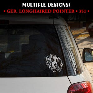 May include: A white vinyl decal of a German Longhaired Pointer dog is affixed to the rear window of a white car. The decal features the dog's head and shoulders in a detailed, stylized design. The text "MULTIPLE DESIGNS!" and "GER. LONGHAIRED POINTER • 351 •" are visible.
