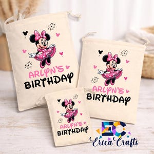 May include: Three beige drawstring bags with a Minnie Mouse design. Each bag features a pink Minnie Mouse illustration, the text "ARLYN'S BIRTHDAY" in pink and black, and decorative accents. The bags vary in size.