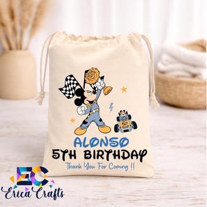 May include: A beige drawstring bag featuring a cartoon Mickey Mouse holding a checkered flag and a trophy. The bag is personalized with the name "Alonso" and the text "5th Birthday". A small race car is also depicted.