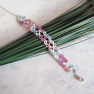 May include: A delicate bracelet made of colorful crocheted thread. The bracelet features a series of small, interconnected loops in shades of pink, blue, and white. The bracelet is secured with a silver clasp.