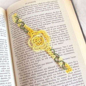 May include: A yellow and green crocheted bookmark with a floral design. The bookmark is placed on a page of a book with text about a medieval castle.