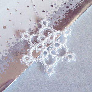 May include: A delicate white snowflake ornament made of crocheted thread, hanging from a silver string.