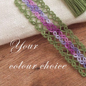 May include: A decorative lace trim featuring an intricate knotted pattern in shades of olive green, magenta, and lavender. The trim is displayed alongside a white fabric swatch and a green tassel. The text "Your colour choice" is overlaid on the image.