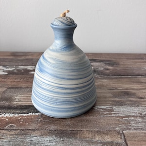 May include: A blue and white ceramic bottle with a swirl design. The bottle has a cork stopper and is sitting on a wooden surface.