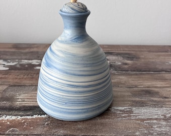 May include: A blue and white ceramic bottle with a swirl design. The bottle has a cork stopper and is sitting on a wooden surface.