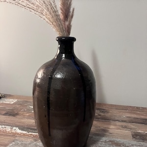 Può includere: Un vaso in ceramica marrone scuro con strisce verticali nere, che contiene un mazzo di erba della pampa secca.