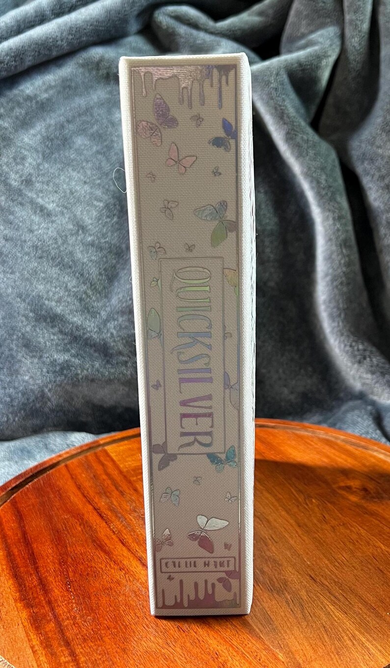 May include: A white box with a holographic design featuring butterflies and the text "Quicksilver" and "Cellie Hunt".