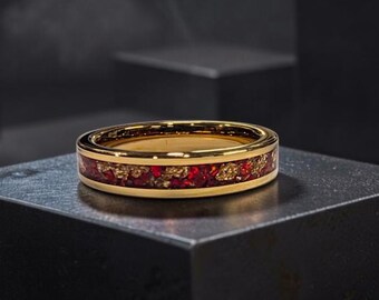 May include: A gold-toned ring featuring a central inlay of crushed deep red and metallic gold fragments. The band has a polished finish with smooth edges, showcasing a vibrant contrast between the metallic gold metal and the textured red inlay.