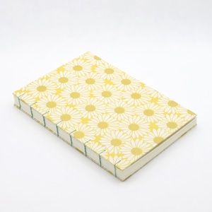 May include: A rectangular notebook with a yellow daisy pattern cover. The notebook is bound with green thread and has a white background. The cover features a repeating pattern of white daisies on a yellow background.