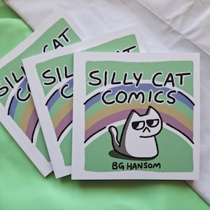 Könnte beinhalten: Drei quadratische Taschenbücher mit dem Titel Silly Cat Comics von BG Hansom. Das Cover zeigt eine weiße Cartoon-Katze mit skeptischem Gesichtsausdruck vor einem mehrfarbigen Regenbogen auf hellgrünem Hintergrund mit schwarzem Text.