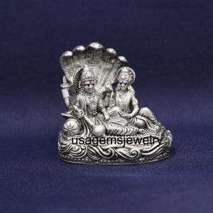 May include: A silver-colored statue depicting two figures seated on a decorative base, with a multi-headed serpent hood behind them. The statue has intricate details and the text "usagemsjewelry" is visible.