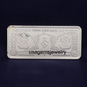 Puede incluir: Una barra rectangular de plata con grabados intrincados. La barra presenta figuras religiosas, diseños florales y texto, incluyendo "50" y "AG99999". La barra también tiene el texto "usagemsjewelry".