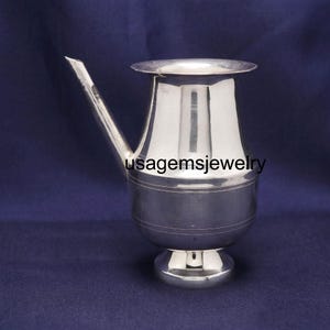 Może przedstawiać: Srebrny metalowy dzbanek z dzióbkiem i szerokim brzegiem. Dzbanek ma pękaty korpus i małą, okrągłą podstawę. Tekst "usagemsjewelry" jest widoczny na korpusie. Tło jest ciemnoniebieskie.
